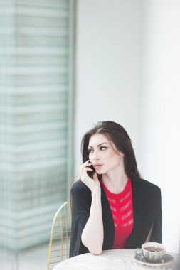 kırmızı siyah kostüm güzel kız masanın kafede kahve sabah fincan ile cep telefonuyla çağırır