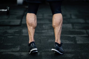 trained legs with muscular calves in sneakers in training gym during hard fitness and crossfit workout
