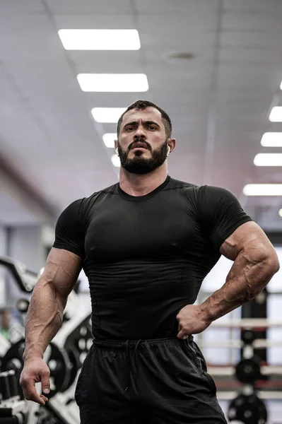Strong handsome young caucasian sport man physique in black sportswear indoor athletic gym posing — ストック写真