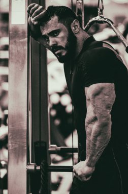 Siyah spor giyim giymiş güçlü, sakallı bir adamın büyük trisepsli kaslarını gösteren klasik bir fotoğrafı.