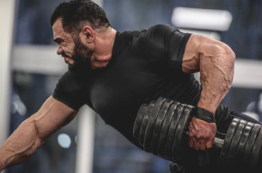 güçlü sakallı adam spor salonunda antrenman yapıyor.