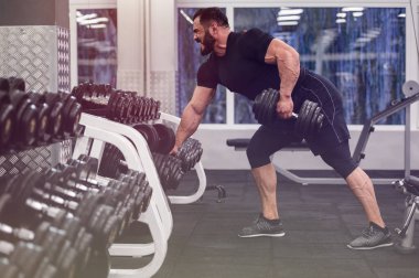 Siyah forma ve şort giyen sakallı güçlü genç adam kaldırıyor.