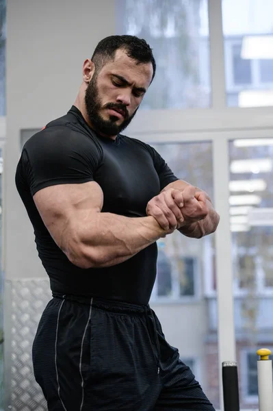 Young bearded strong man in black sportswear showing muscle of b — Zdjęcie stockowe