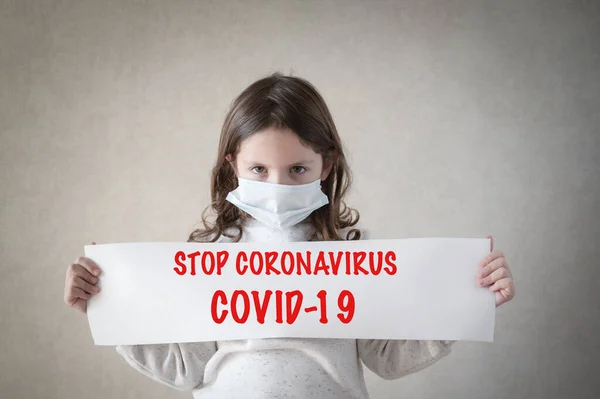 Opieka zdrowotna covid-19 epidemia koncepcja epidemii małej dziewczynki w masce medycznej trzymając papierowy baner z hasłem stop koronawirus czerwony tekst — Zdjęcie stockowe