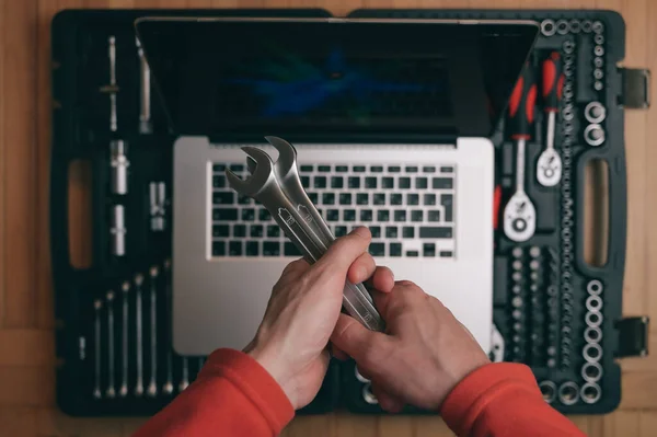 Computer vedligeholdelse reparation koncept af mand tekniker holder krom sokkel skruenøgle spanner på baggrund med sølv laptop på auto værktøjskasse kit i værksted - Stock-foto