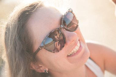 Mutlu gülümseyen genç anne, oğlunun koruyucu kaskını takmak için güneş gözlüklerine yansıyan oğlunu destekliyor.