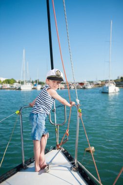 Kaptan beyaz şapkalı ve kot şortlu şirin çocuk yaz gezisi sırasında limanda lüks deniz yatında dikiliyor.