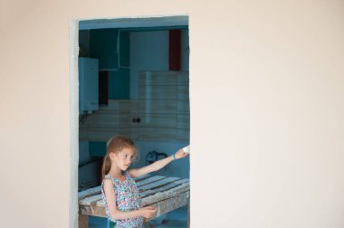 home reconstruction concept of beautiful little girl painter with paint brush in hand in house room during repair overhaul clipart