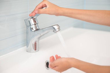hands opening faucet with water in bathroom clipart
