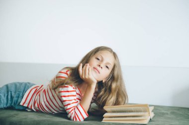 Güzel küçük kız kanepede uzanıp kitap okuyor.