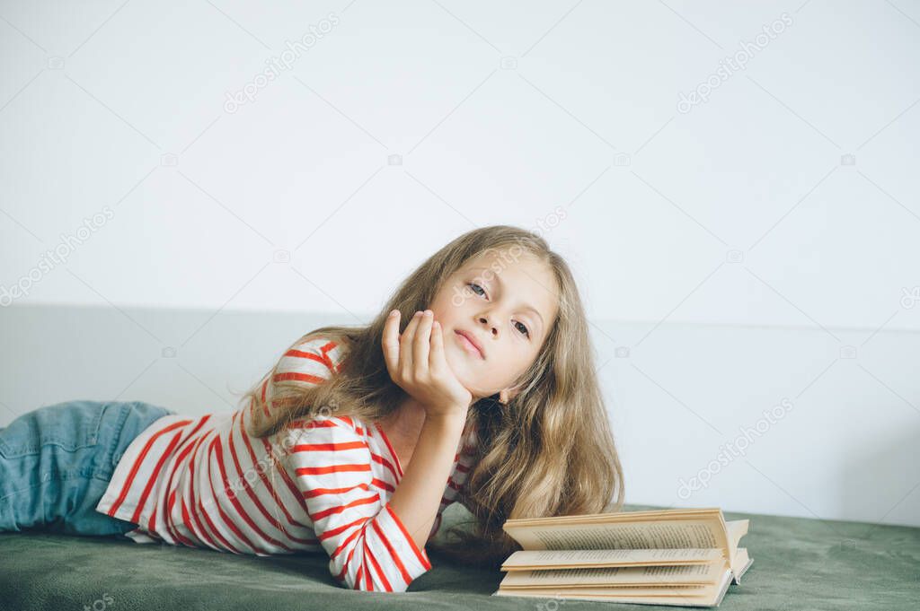 beautiful little girl lying on sofa reading book