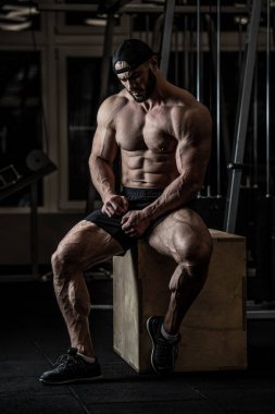 Sakallı, kasketli ve şortlu yakışıklı genç adam antrenman sırasında tahta kutunun üzerinde oturuyordu.