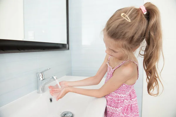 Красивая кавказская маленькая девочка с длинными волосами, моющие руки со свежей водой в ванной комнате — стоковое фото