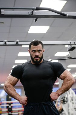 Siyah formalı güçlü genç adam spor salonunda spor yaparken kaslarını gösteriyor.