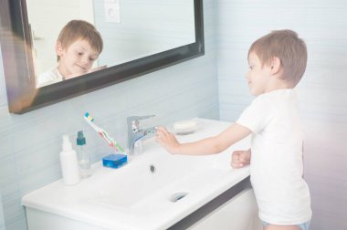 Beyaz kolsuz tişörtlü yakışıklı beyaz çocuk parlak mavi banyodaki leğende dikiliyor.