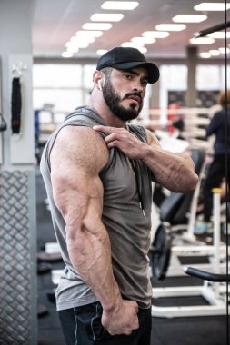 Spor salonunda poz verirken kaslarını gösteren sakallı güçlü bir adam.
