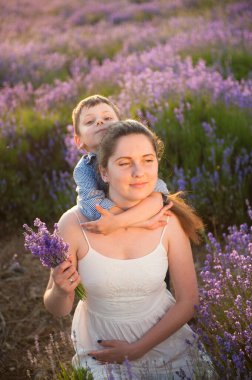 Mutlu bir aile gülümseyen küçük bir çocuk beyaz elbiseli güzel annesine sarılıyor. Mor çiçekli yaz çayırlarında bir demet lavanta koyuyor.