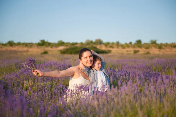 Happy smiling family caucasian beautiful mother and embracing small kid in summer blooming flower field during leisure vacation — Stock Photo, Image