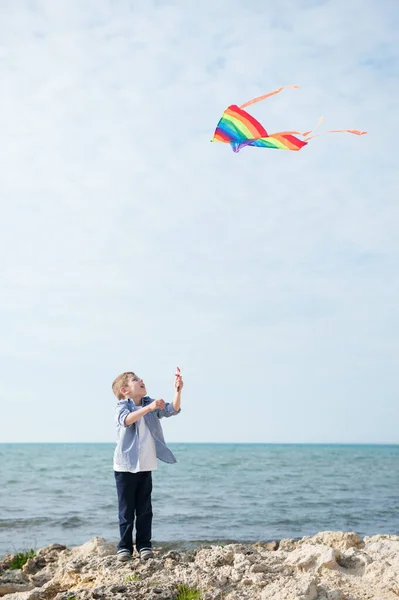 Piccolo bambino caucasico attivo controllo aquilone volante in cielo blu sulla riva del mare in giorno d'estate — Foto Stock