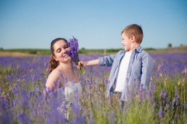 Mutlu küçük beyaz çocuk çiçek açan tarlada gülümseyen annesine lavanta çiçeği buketi veriyor.