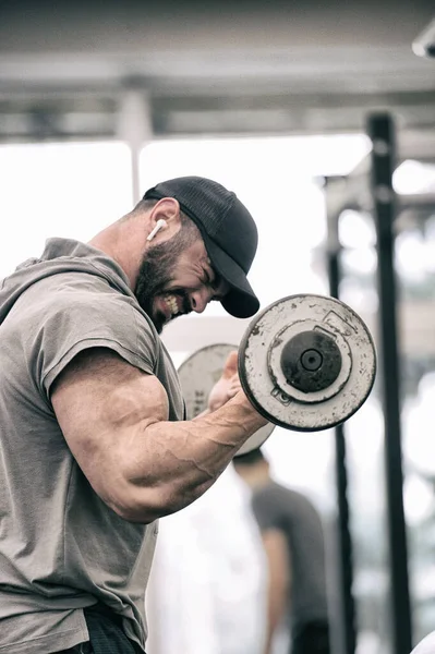 sport motivation concept of strong young athlete man with beard lifting weight barbell pumping iron training biceps with angry emotions pushing to limits