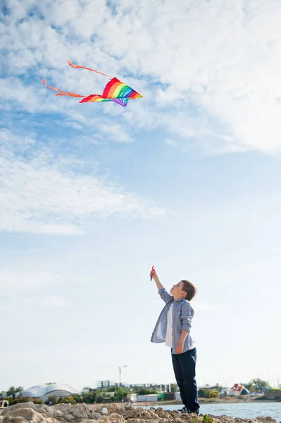 Sport piccolo ragazzo caucasico con volare aquilone multicolore su sfondo cielo blu il giorno d'estate — Foto Stock