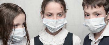Coronavirus COVID-19 karantinası sırasında maskeli ve okul üniformalı üç küçük çocuk.