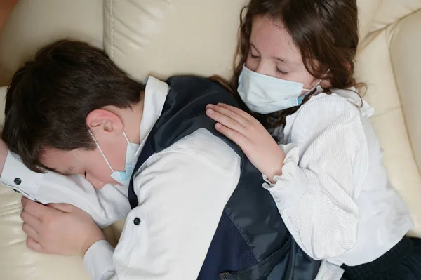 Wirus coronavirus covid-19 epidemia wybuchu kwarantanny koncepcja dwóch dzieci w ubraniach szkolnych leżących śpiących na kanapie cierpiących na ból — Zdjęcie stockowe