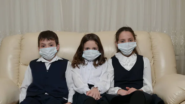 two little sick kids in school uniform wearing medical mask sitting at home during coronavirus covid-19 quarantine
