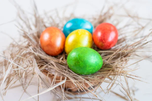 Multi-colored Easter eggs lie on a straw in the form of a nest in a basket on a white background. Happy easter