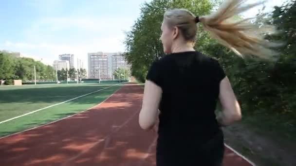 La giovane donna corre su una pista da corsa. bionda — Video Stock