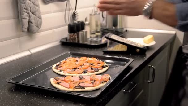 Человек готовит пиццу на кухне дома. посыпать тертым сыром — стоковое видео