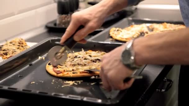 Ein Mann schneidet eine heiße Pizza auf dem Küchentisch — Stockvideo