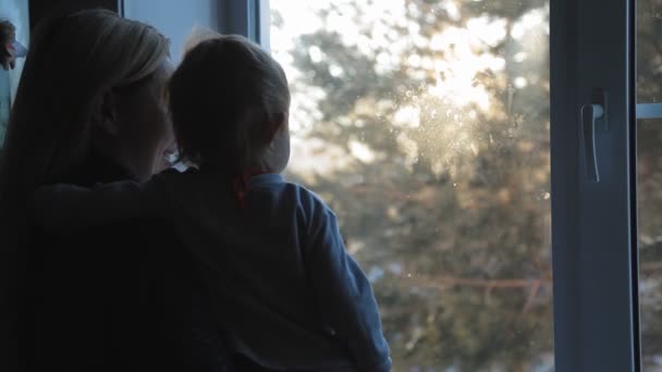 Mujer rubia joven con un niño pequeño de pie en la ventana y disfrutar de la mañana helada — Vídeo de stock