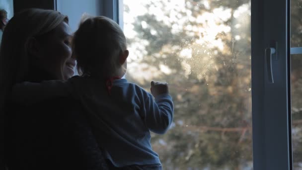 Ung blond kvinna med ett litet barn står vid fönstret och njuta av frostiga morgonen — Stockvideo