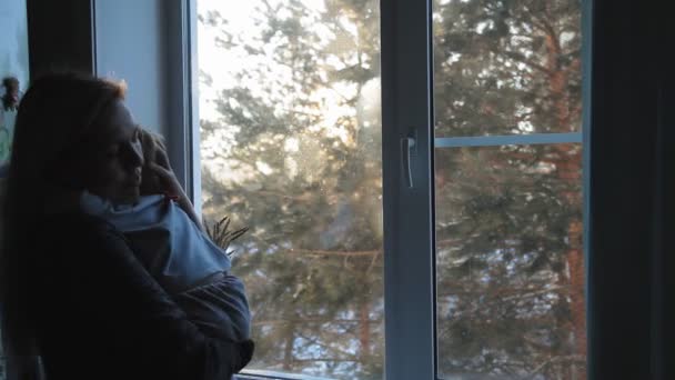 Mujer rubia joven con un niño pequeño de pie en la ventana y disfrutar de la mañana helada — Vídeos de Stock
