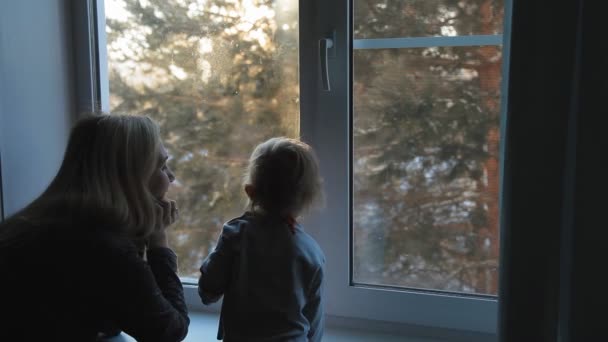 Mujer rubia joven con un niño pequeño de pie en la ventana y disfrutar de la mañana helada — Vídeos de Stock