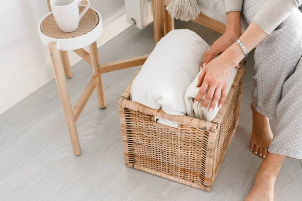 Primer plano, las manos de una mujer doblan una tela escocesa en una cesta de madera. Organización del espacio en la casa. Material natural Imágenes de stock libres de derechos