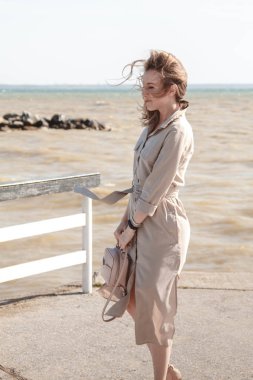 Bej elbiseli güzel sarışın denizi seviyor. Seyahat etme özgürlüğü, doğanın tadını çıkarma, dalgalı saçlarındaki rüzgar....