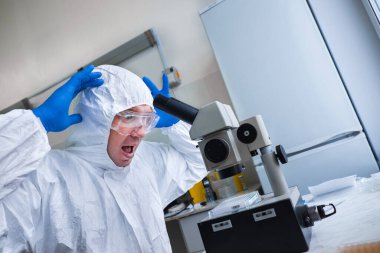 Beyaz koruyucu kıyafetli ve gözlüklü bir biyolog laboratuarda mikroskop ile çalışıyor. Bilim adamı şaşırdı ve korktu. Korkunç bir virüs. Salgın ve salgın konsepti