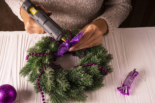 Женские руки украшают рождественский венок декором с помощью клеевого пистолета
.