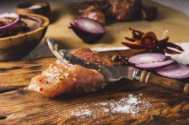 Baharatlı barbekü eti, bıçak, tuz ve biber, mutfak tahtasında. Beyaz arka planda eti olan ahşap kase..