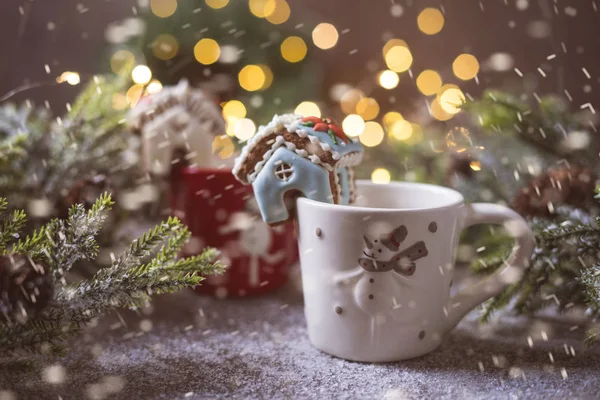 Miniature gingerbread house on a chpshka against the background of a Christmas tree of fire garland. Snowfall effect.