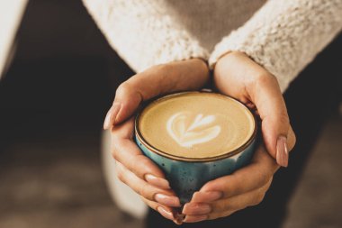 Güzel kadın elleri kapuçinolu mavi bir kupa tutuyor..