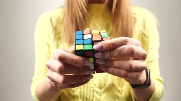 Kvinna i en gul stickad tröja som håller rubiks kub och leker med den. Rubiks kub i kvinnliga händer, närbild. 4k — Stockvideo