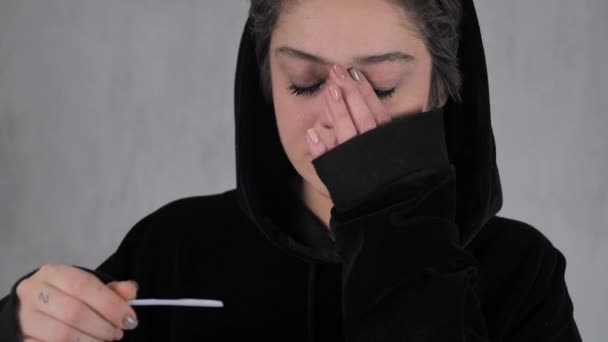 Unglückliche schwangere Teenager kurzhaarig in einem schwarzen Kapuzenpulli mit positivem Geburtenkontrolltest. 4k — Stockvideo