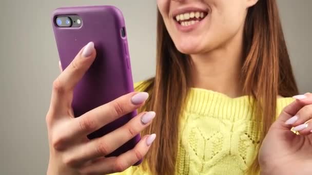 Mujer se comunica por Skype a través de teléfono inteligente. Ella está usando un suéter amarillo brillante — Vídeo de stock