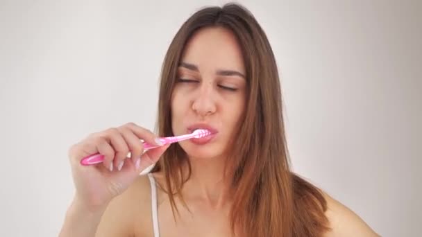 Retrato de una mujer joven que se cepilla los dientes después de despertar sobre un fondo blanco. Concepto de higiene. 4k — Vídeo de stock