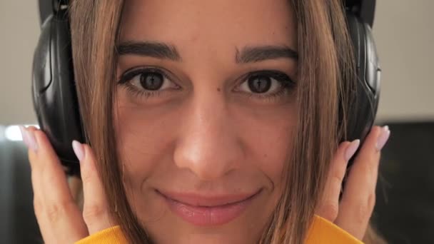 Close-up portrait of a girl who listens to music in headphones. Girl looking directly at the camera — Stock Video