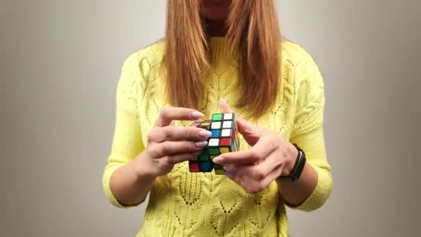 Femme dans un pull tricoté jaune tenant rubiks cube et jouer avec elle. Rubiks cube dans les mains des femmes, fermer. 4k — Video